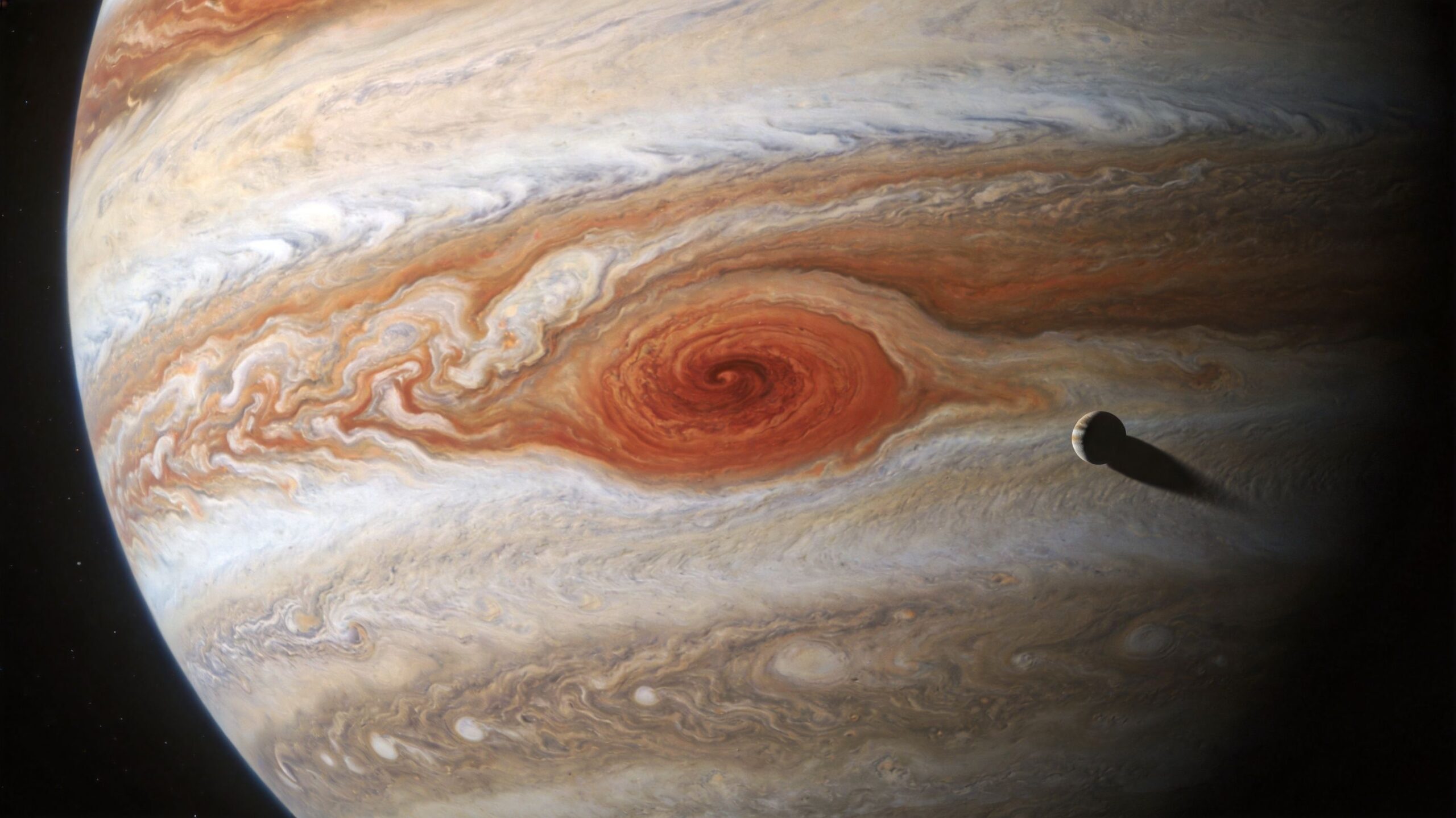 A close-up view of Jupiter with its Great Red Spot and a moon casting a dark shadow.